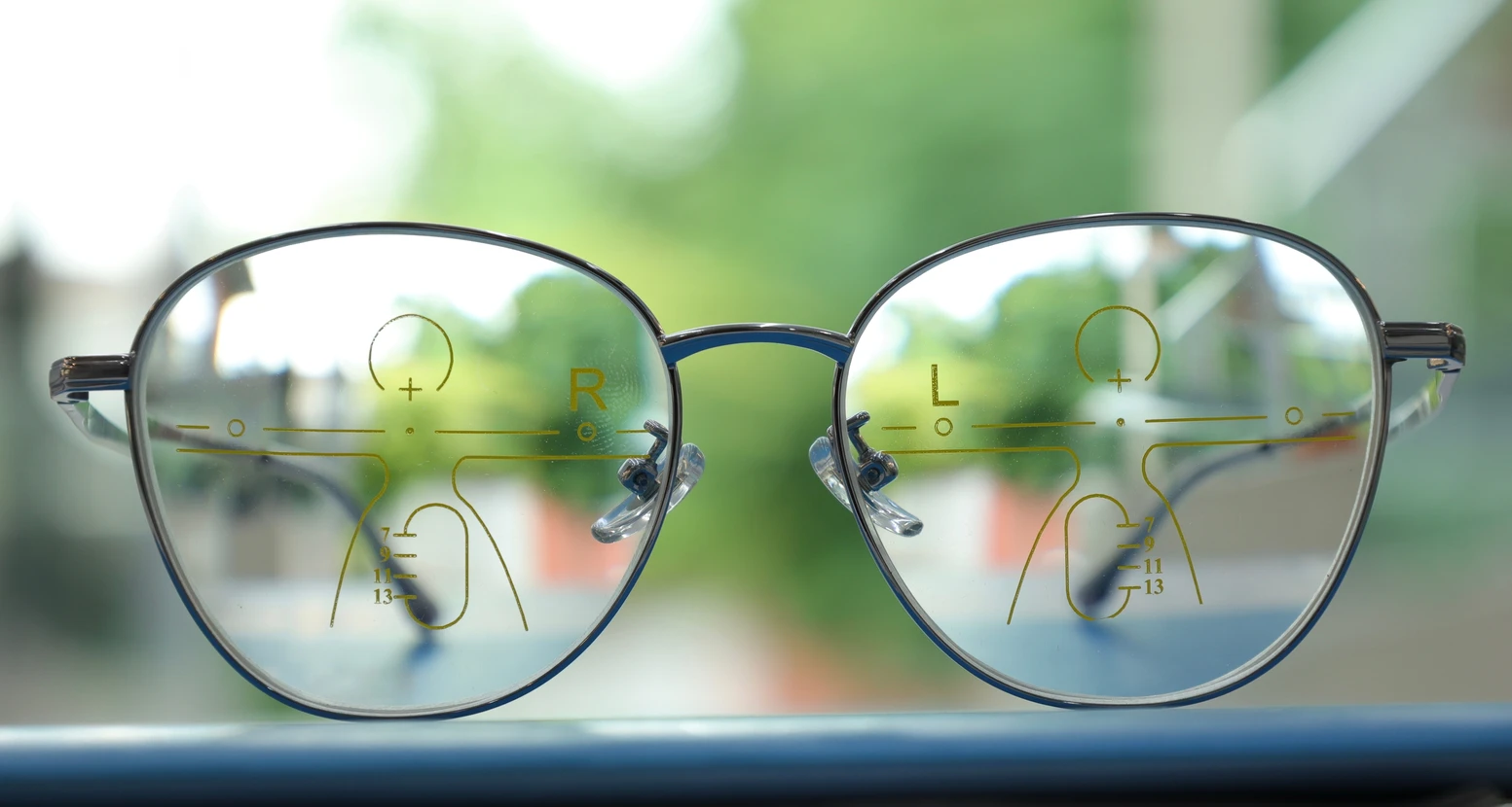 Lunettes progressives posées sur surface bleue avec arrière-plan flou verdoyant