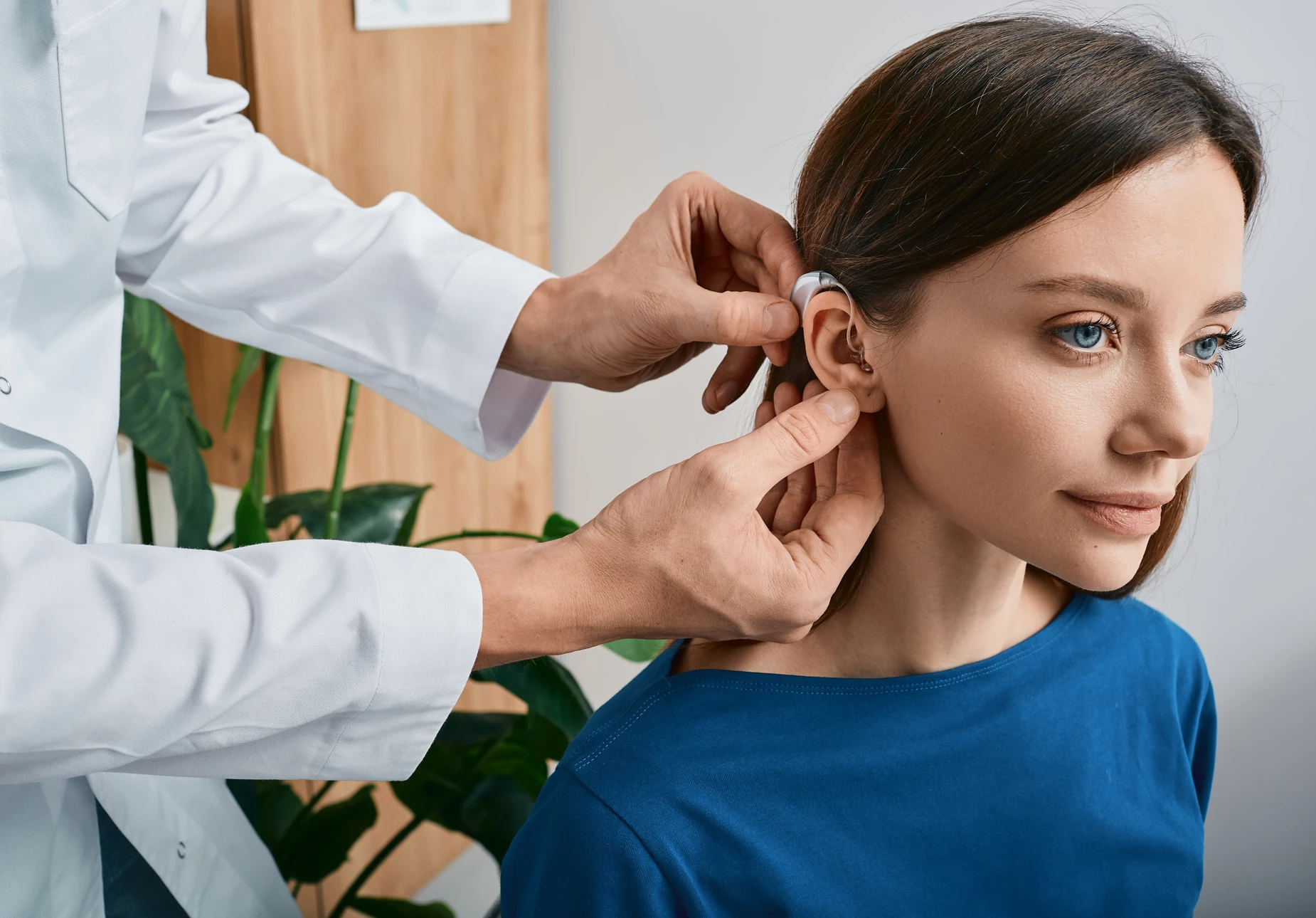 Professionnel de santé en blouse bleue présentant un appareil auditif intra-auriculaire dans un cabinet médical moderne
