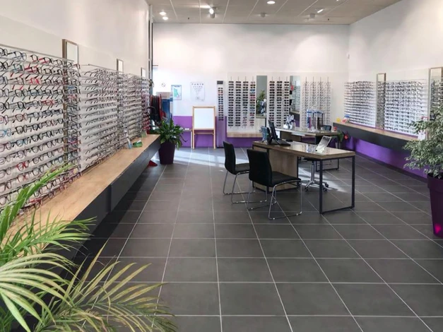 Un opticien afro-américain, debout à la vue, fait bon ménage avec un sourire sur le visage pointant de la main et du doigt vers le côté avec une expression heureuse et naturelle